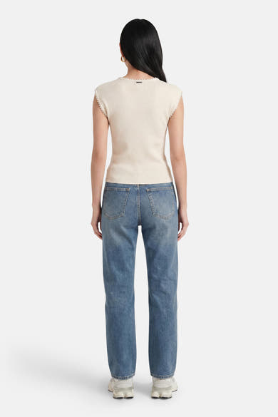 T-shirt côtelé beige de GOA GOA, à bordures festonnées et étiquette métallique, vue de dos, porté avec un jean bleu et des baskets.