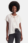 Witte GOA GOA blouse, ronde hals versierd met een gouden ketting en kleurrijke kwastjes, korte wijde mouwen, gedragen met een donkere jeans.
