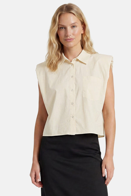Chemisier sans manches beige de GOA GOA avec col, boutonnage, poche poitrine, porté avec une jupe noire.