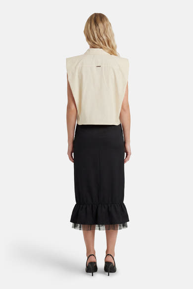 Chemisier sans manches beige de GOA GOA avec petite plaque dorée au dos, porté avec une jupe noire à volants en tulle, vue de dos.