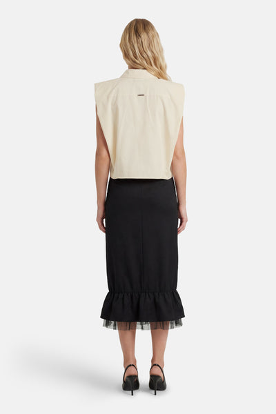 Chemisier sans manches beige de GOA GOA avec petite plaque dorée au dos, porté avec une jupe noire à volants en tulle, vue de dos.