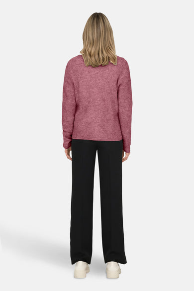 Roze V-hals trui van ONLY, gedragen met een zwarte broek en sleehakken.