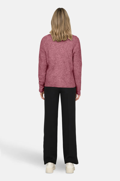 Roze V-hals trui van ONLY, gedragen met een zwarte broek en sleehakken.