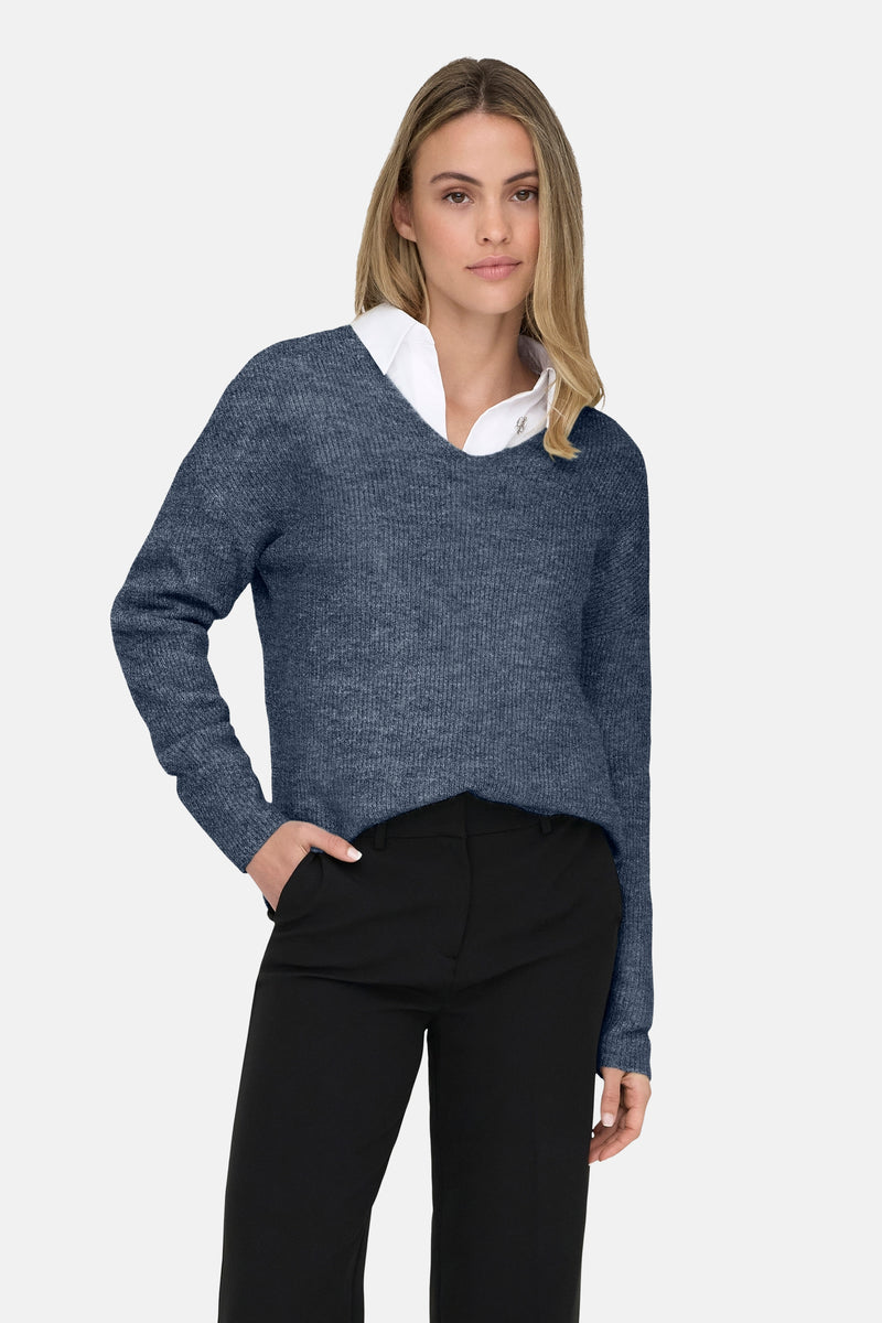 Blauwe V-hals trui van ONLY, gedragen over een wit overhemd en een zwarte broek.
