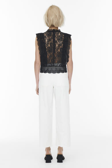 Blouse noire sans manches de ONLY®, avec motif en dentelle, portée avec un pantalon blanc et des mules noires.