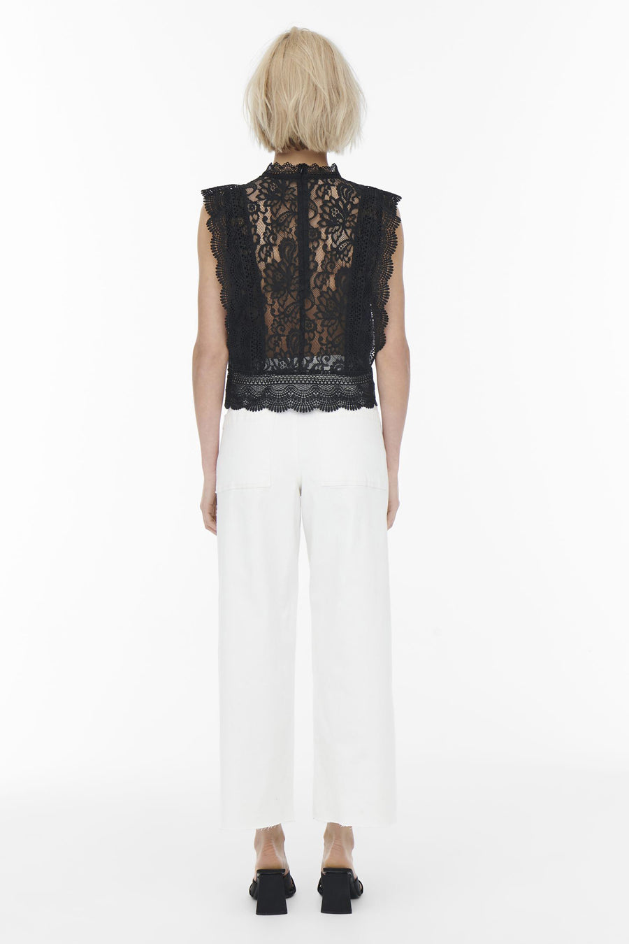 Blouse noire sans manches de ONLY®, avec motif en dentelle, portée avec un pantalon blanc et des mules noires.