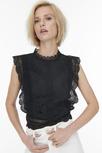 Blouse sans manches noire de ONLY, en dentelle florale avec col montant festonné, portée avec un pantalon blanc.