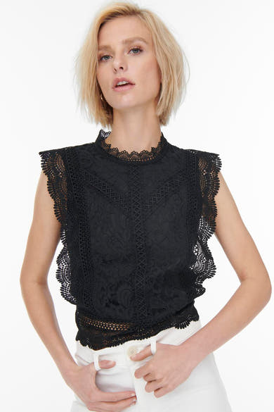 Blouse noire en dentelle de ONLY®, à col montant et à bordures festonnées, portée avec un pantalon blanc.
