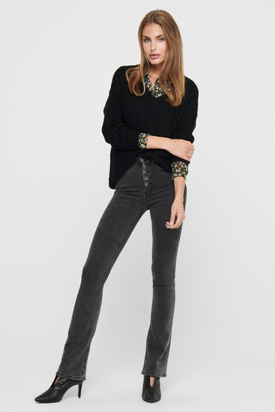 Pull col V noir de JDY, porté sur une chemise imprimée et un jean gris foncé à taille haute.
