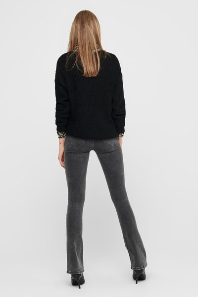 Pull noir à maille épaisse de JDY, porté avec un chemisier à fleurs et un jean gris.