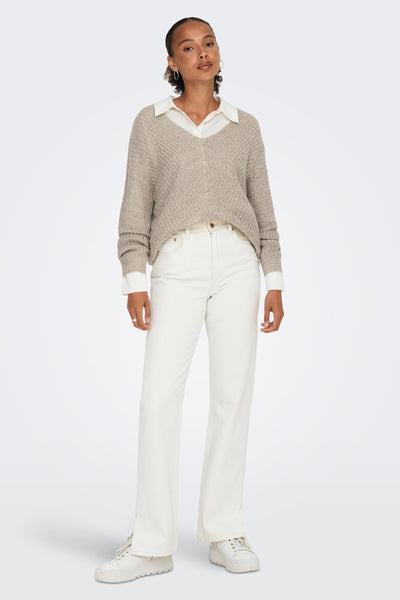 Pull col V brun de JDY porté avec une chemise blanche et un jean blanc à jambes évasées.