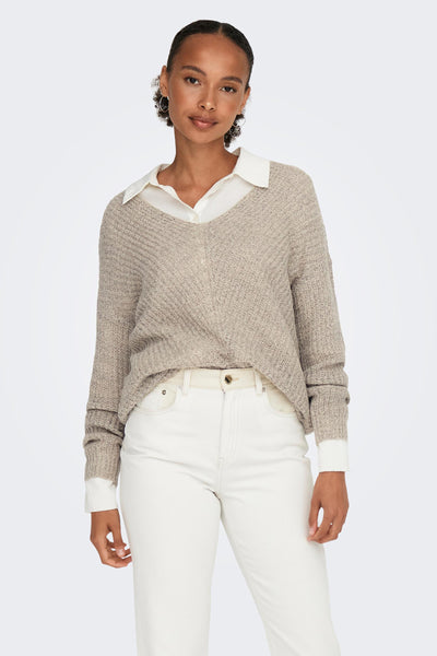 Pull à col V brun de JDY porté sur une chemise blanche avec un pantalon blanc et une ceinture crème.
