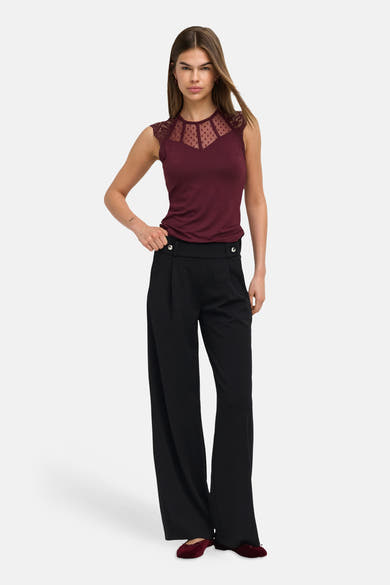 Black wide-leg elastic waist trousers with front pleats and button details, worn with burgundy top and matching shoes, full-length front view
