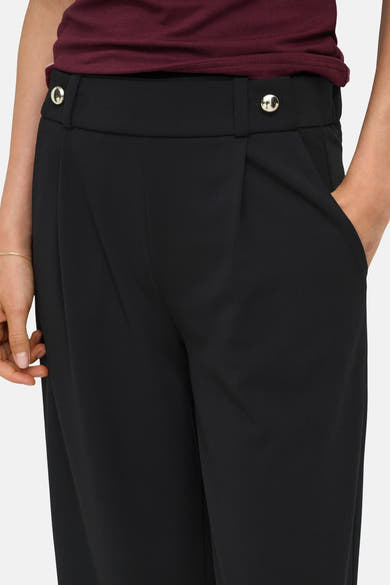 Black elastic-waist women's trousers with front pleats and silver-toned buttons, worn with a burgundy top, side view