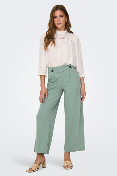 Pantalon de costume vert olive de JDY, porté avec un chemisier blanc et des mules à talons.
