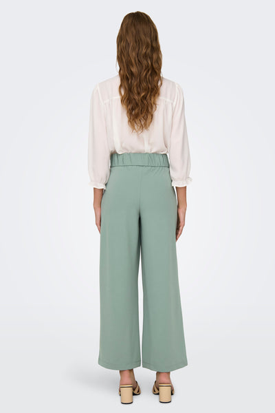 Pantalon costume vert de JDY, coupe large, avec élastique à la taille et chaussures à talons beiges.
