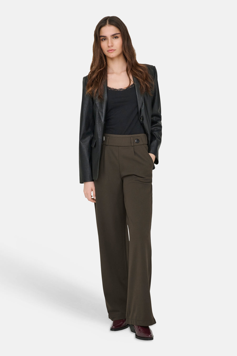 Pantalon de costume brun de JDY, avec une taille haute et une jambe large, porté avec un chemisier noir et un blazer en cuir.