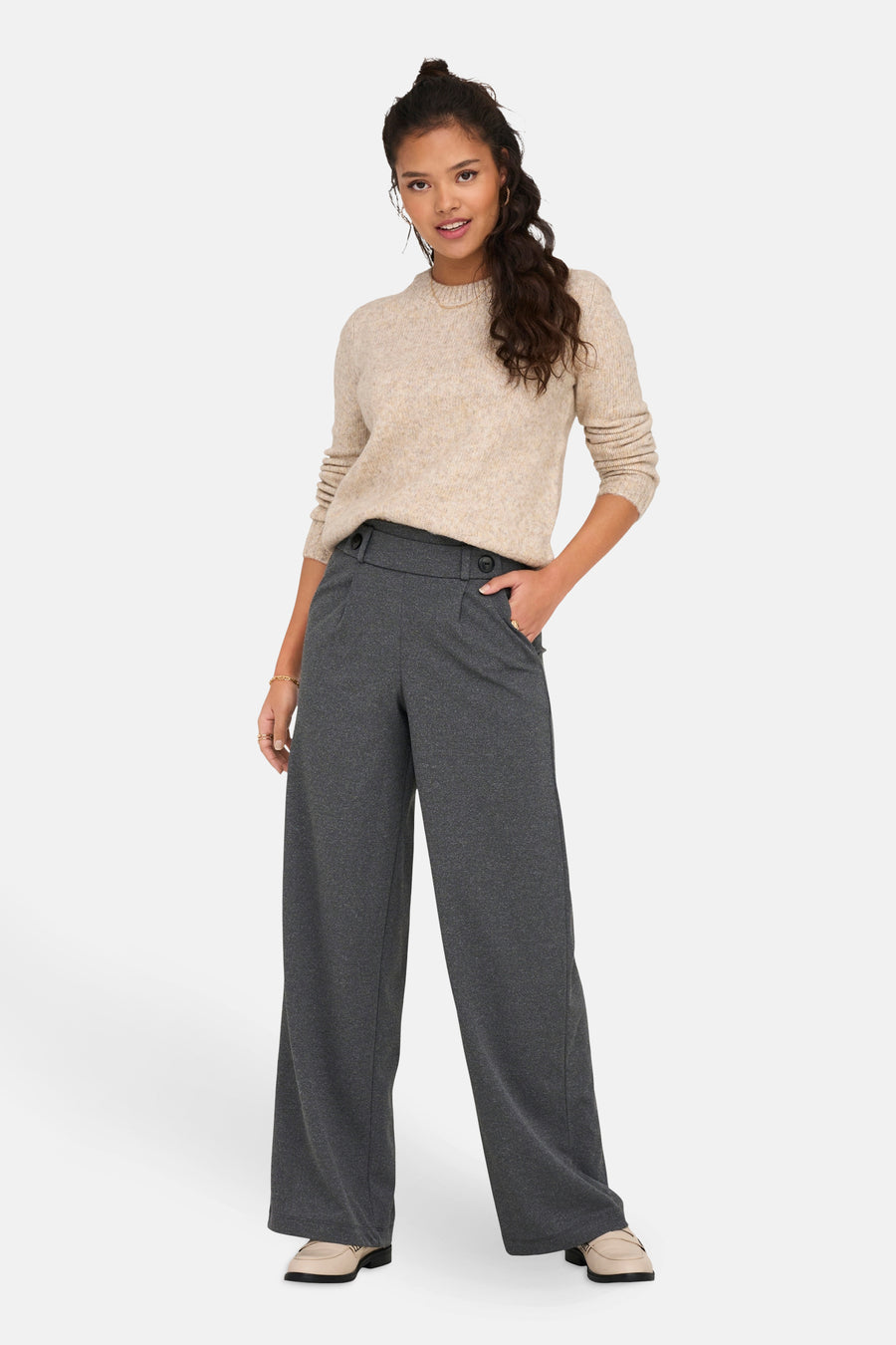 Pantalon de costume gris de JDY, coupe ample avec taille haute à boutons, porté avec un pull beige.
