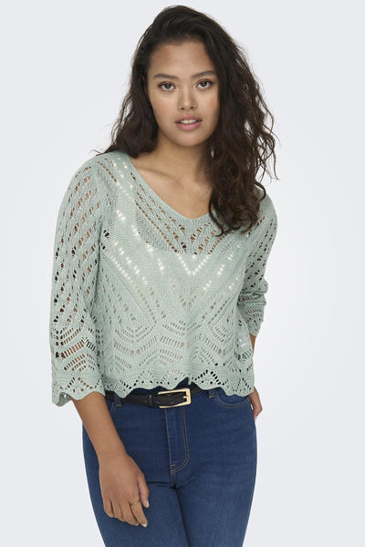 Pull à col en V vert de JDY avec motif ajouré, porté avec un jean et une ceinture noire.
