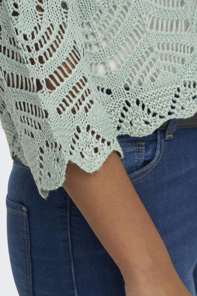 Pull à col en V vert de JDY, avec motif ajouré, porté avec un jean bleu.