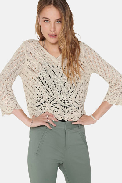Pull col V beige de JDY, en maille ajourée avec motif chevron, porté avec un pantalon vert.
