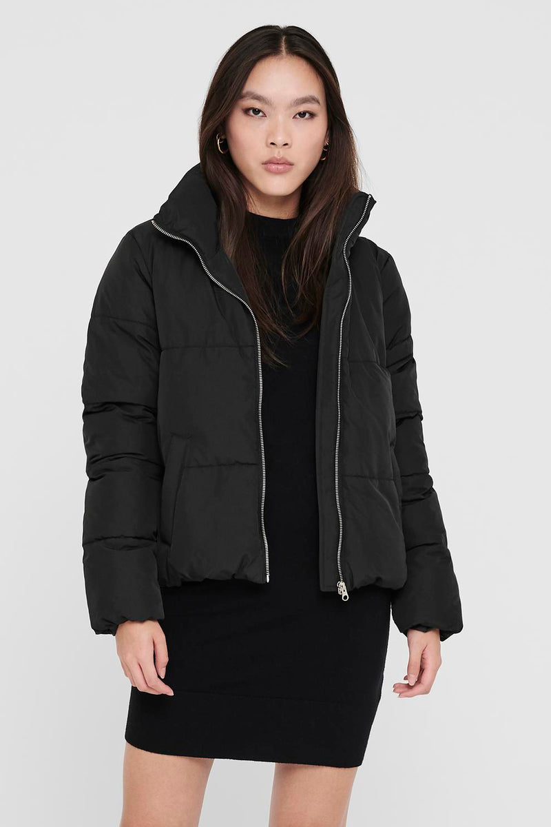 Black quilted puffer jacket with high collar and silver zipper, front view on model wearing black dress