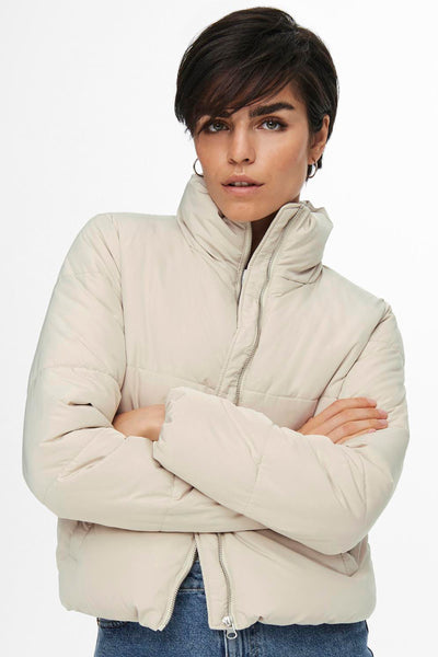 Veste courte écrue de JDY, avec fermeture éclair, manches longues et la femme qui pose avec des boucles d'oreilles créoles.
