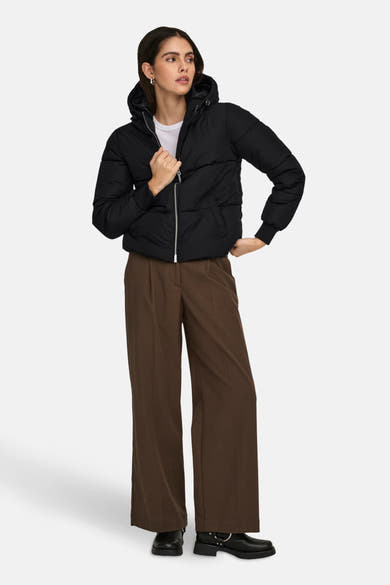 Korte zwarte jas van JDY met capuchon en ritssluiting, gedragen met een bruine broek en zwarte laarzen.