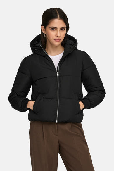 Korte zwarte jas van JDY, met capuchon en zilveren ritssluiting, gedragen met een bruine broek.