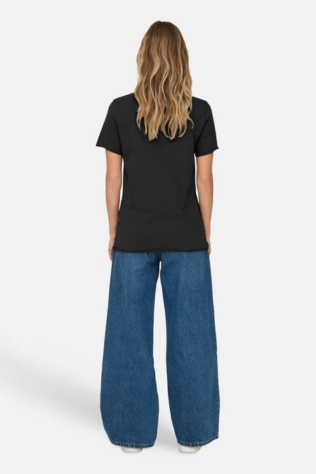 T-shirt gris à manches courtes de ONLY®, porté avec un jean ample bleu et des cheveux longs ondulés.