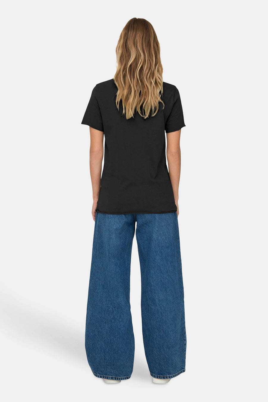 T-shirt gris à manches courtes de ONLY®, porté avec un jean ample bleu et des cheveux longs ondulés.