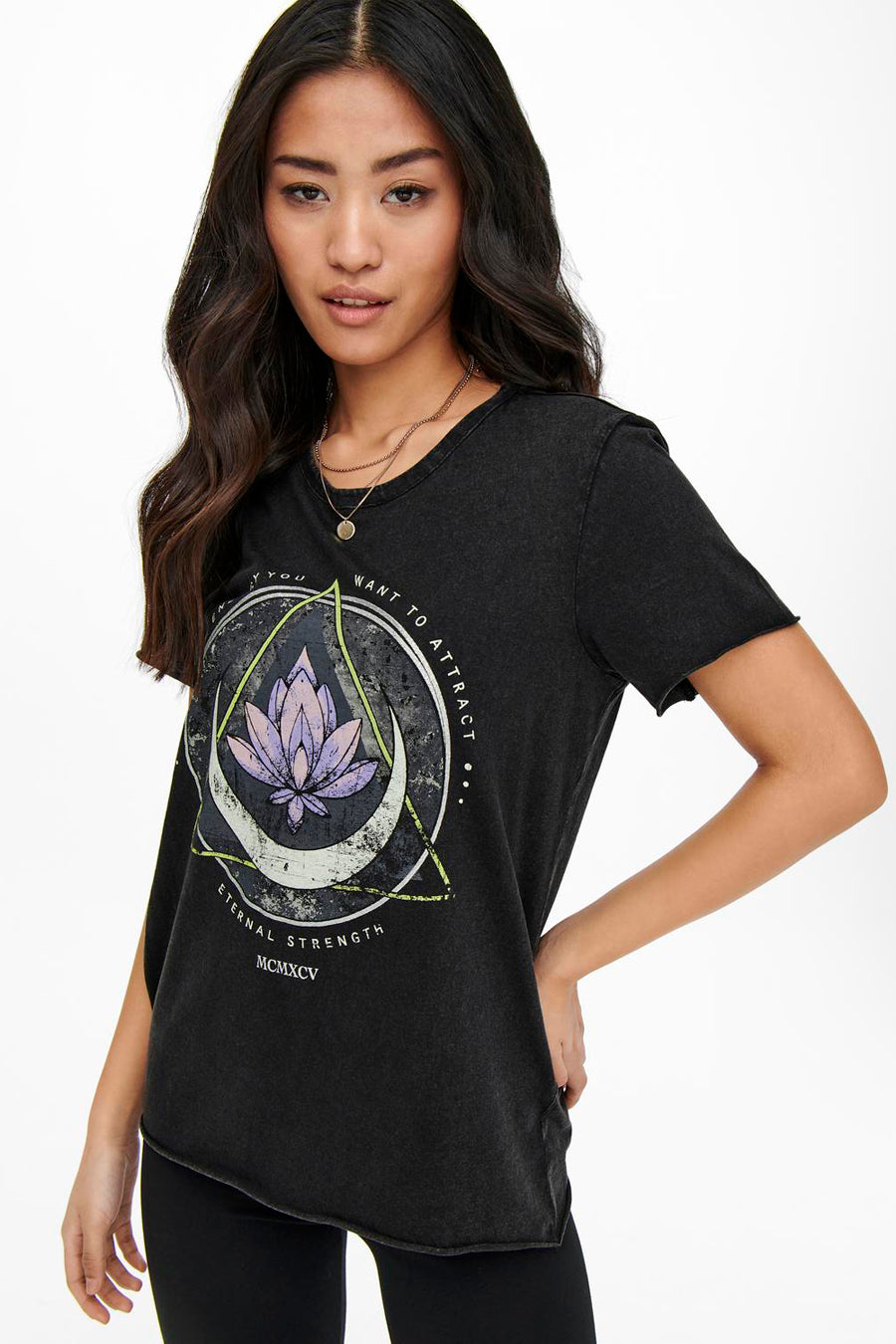 T-shirt noir à manches courtes de ONLY, avec imprimé lotus et texte ésotérique, porté avec un collier fin.
