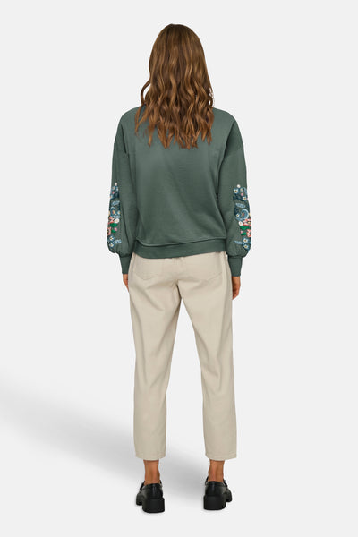 Groene trui met ronde hals van ONLY®, met bloemenborduursels op de mouwen, gedragen met een beige broek.