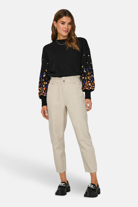 Zwarte trui van ONLY, met lange mouwen versierd met kleurrijke bloemenpatronen, gedragen met een beige broek en zwarte schoenen.