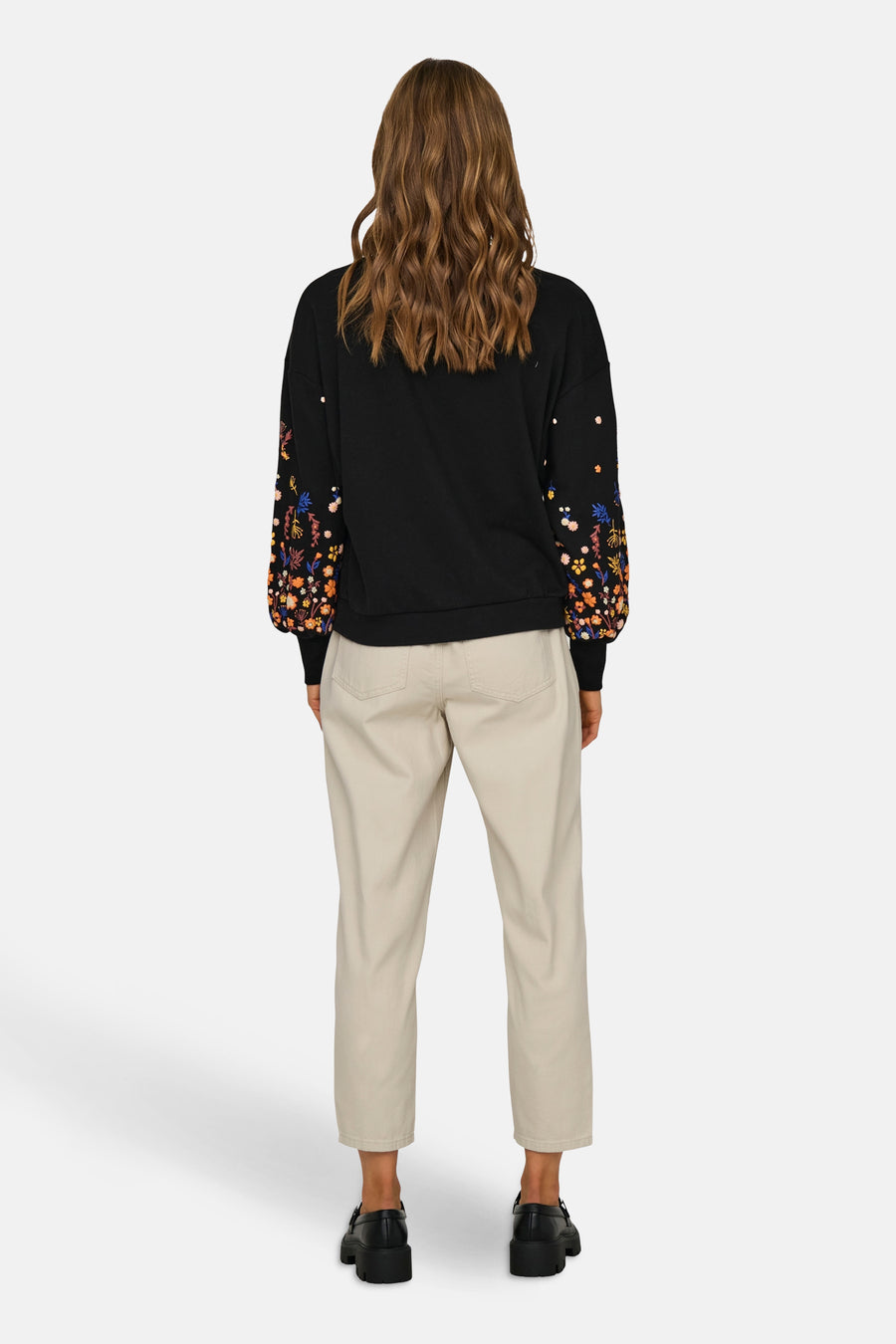 Sweat noir de ONLY®, avec des manches longues fleuries, porté avec un pantalon beige et des chaussures noires.