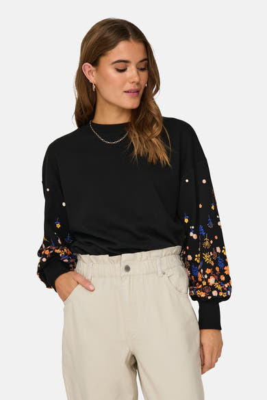 Sweat noir par ONLY® avec manches bouffantes à motifs floraux, porté avec un pantalon beige.

