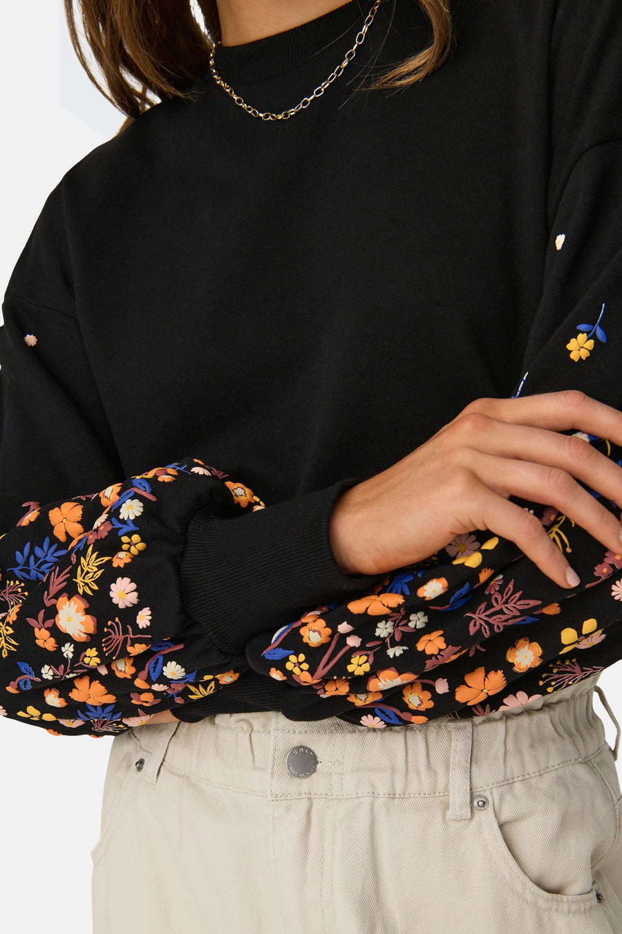Sweat col rond noir de ONLY, manches longues à imprimé floral, porté avec un pantalon beige.
