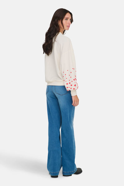 Ecru sweatshirt van ONLY, versierd met patronen van kleine rode hartjes op de mouwen, gedragen met een wijde blauwe jeans.