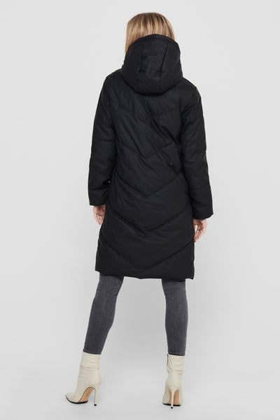 Zwarte lange jas van JDY met een gewatteerd chevronpatroon, gedragen met een grijze jeans en witte enkellaarsjes.
