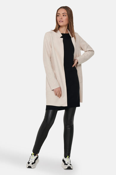 Veste longue beige de ONLY, portée avec une robe noire, un legging en cuir et des baskets chunky.

