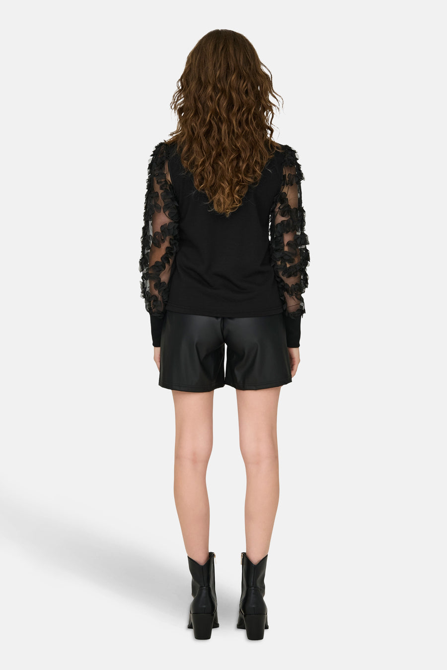 Sweat noir à manches longues de JDY, avec des détails à volants floraux et porté avec des shorts en cuir et des bottes noires.
