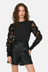 Sweat noir à col rond by JDY, avec manches longues en tulle ornées de motifs floraux, porté avec un short noir taille haute.
