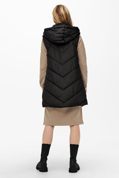 Bodywarmer noir JDY avec capuche, porté sur une robe beige et des bottes noires.