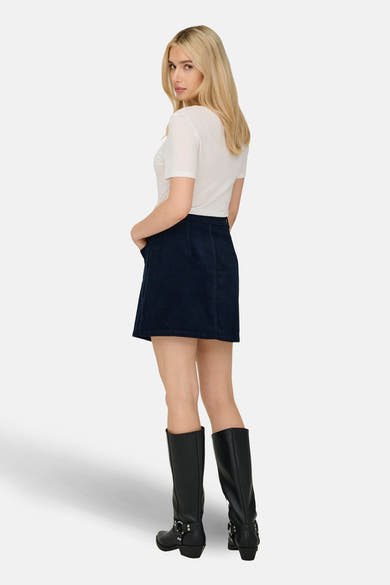 Korte marineblauwe fluwelen rok van JDY, gedragen met een wit T-shirt en zwarte laarzen.