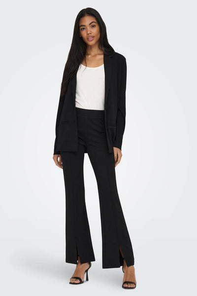 Blazer noir de JDY porté avec un débardeur blanc et un pantalon noir fendu, chaussures à talons.