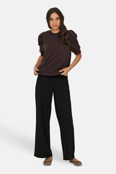 Pantalon costume noir de JDY, coupe large, porté avec un haut marron à manches bouffantes et des ballerines.