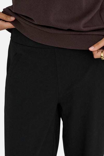 Pantalon costume noir de JDY en tissu lisse, avec poche latérale, porté sous un haut marron.