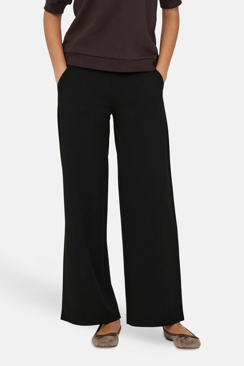 Pantalon costume noir à jambe large de JDY, coupe fluide avec poches, porté les mains dans les poches.