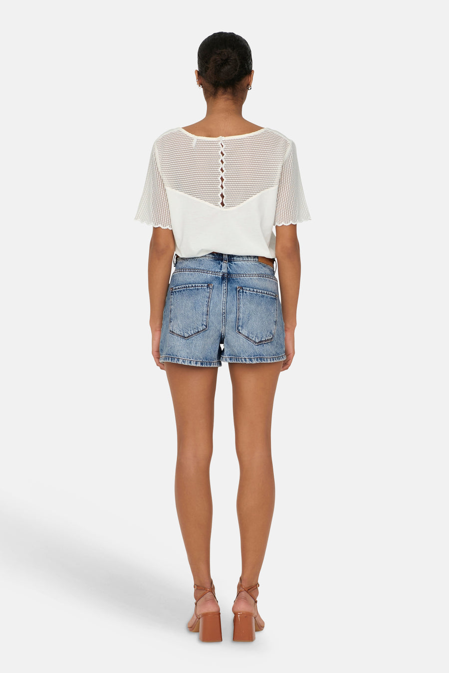 Short en jean bleu moyen de ONLY®, vue de dos, porté avec un haut blanc texturé et des sandales marron à talon carré.