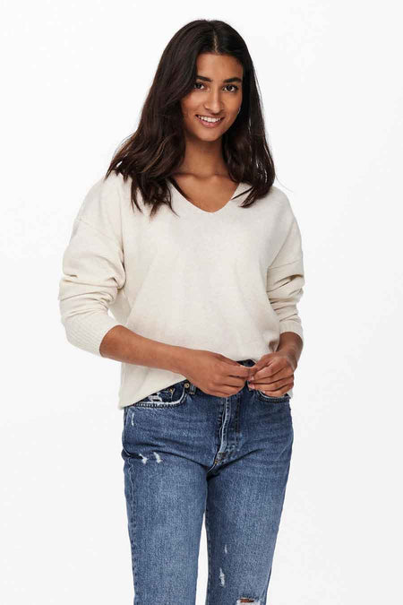 Pull col V écru de ONLY, porté avec un jean bleu délavé.